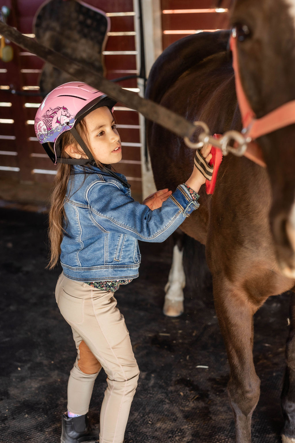Young rider enthusiastically grooming her horse in the barn